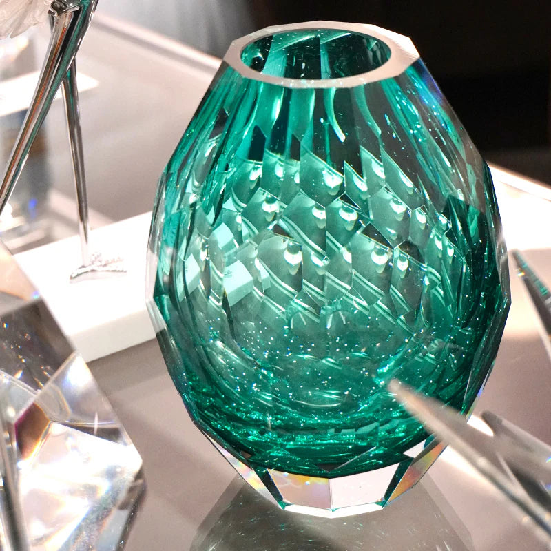 A faceted green glass vase with a textured, diamond-cut pattern and a silver-toned rim, shown on a reflective surface.