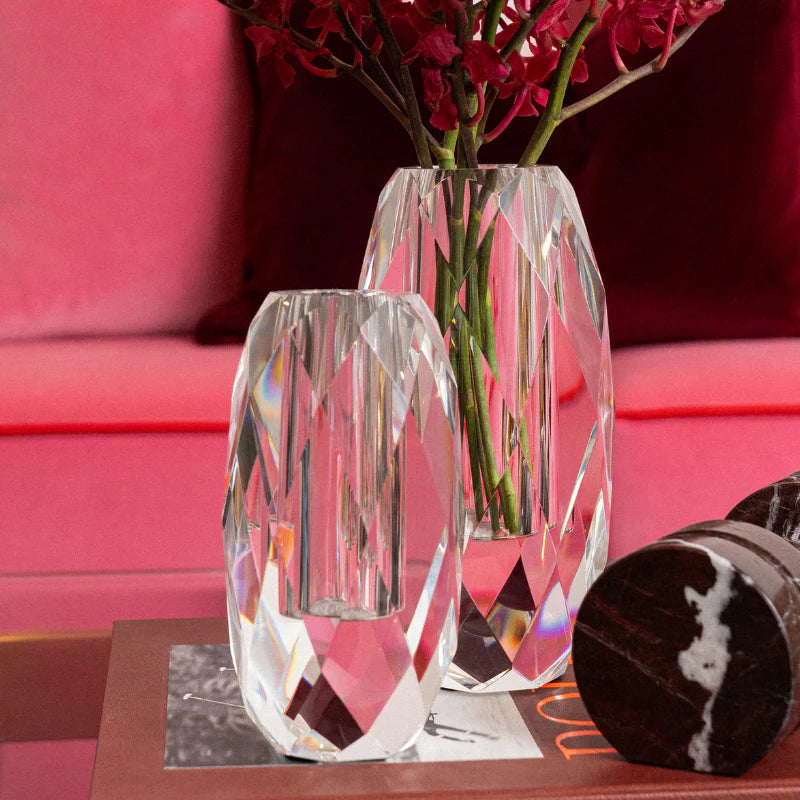 Two crystal vases on a table with a pink couch in the background