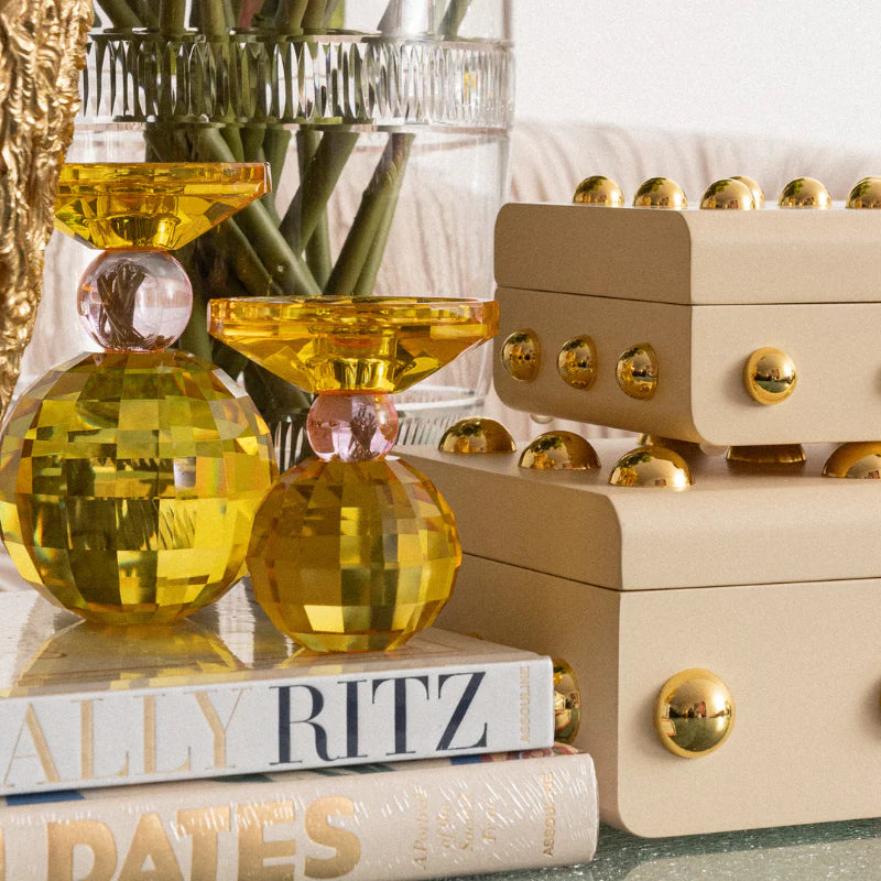 Decorative yellow glass vases on books with a beige box and plant in the background